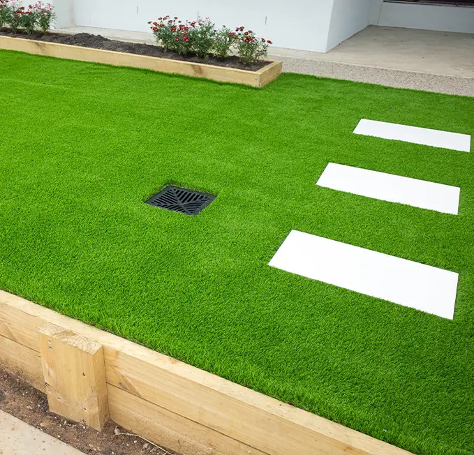Artificial Grass with Pavers and Drainage Lush artificial grass lawn featuring white paver stones and a drainage grate, ideal for landscaping and outdoor design.