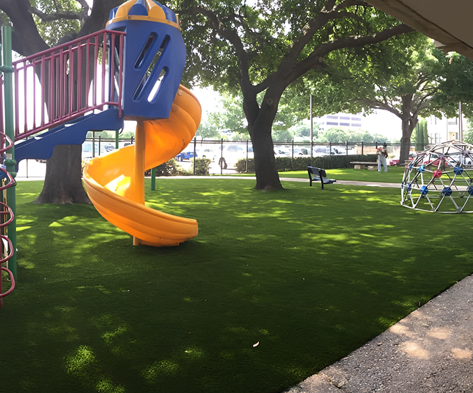 Colorful Playground Slide and Climbing Structure Bright orange slide and climbing dome in a playground with artificial grass, surrounded by trees and open space.